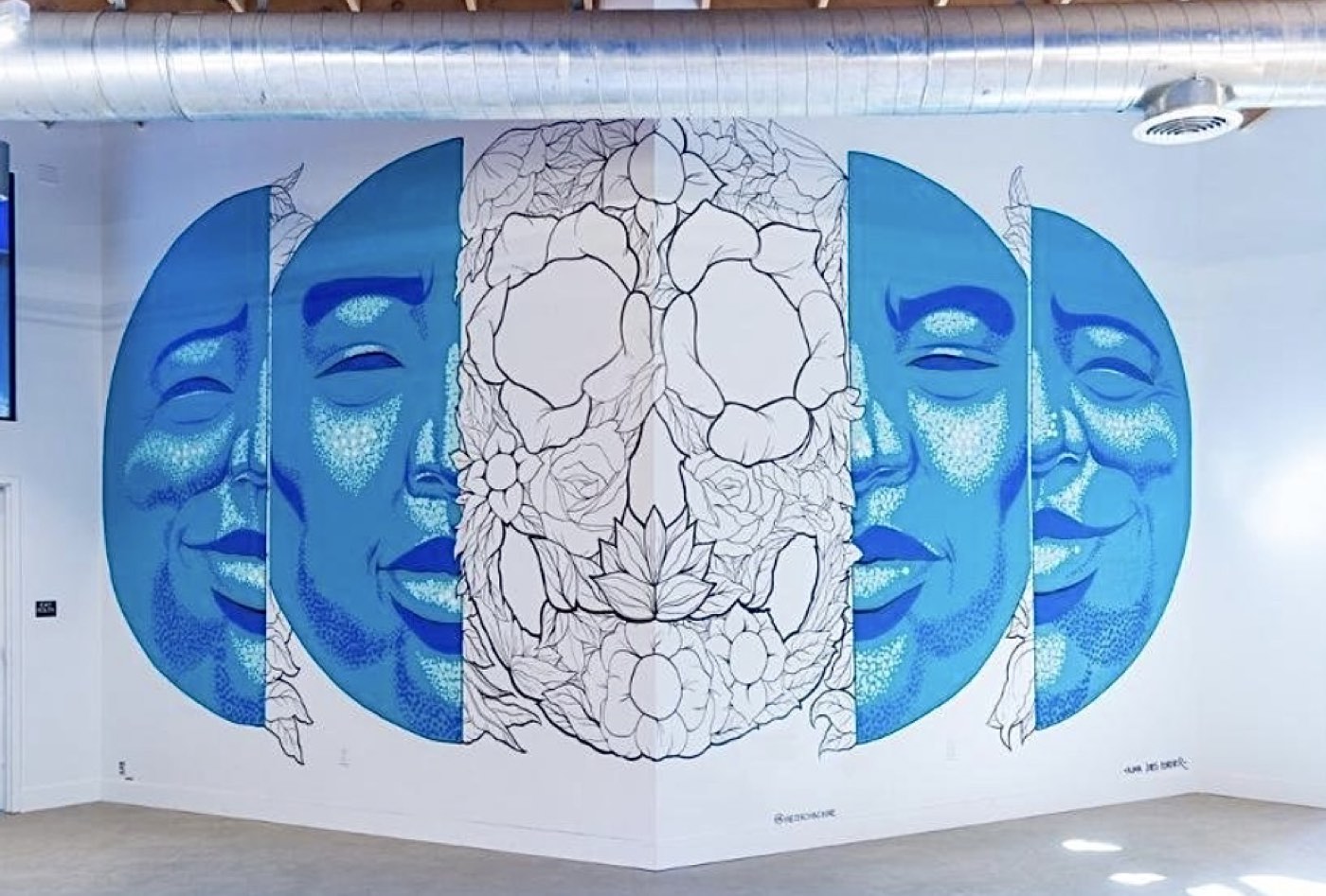 Twin blue moonlit faces wrapping a corner around a line-work floral skull at Catalyst Cannabis in Pomona, California